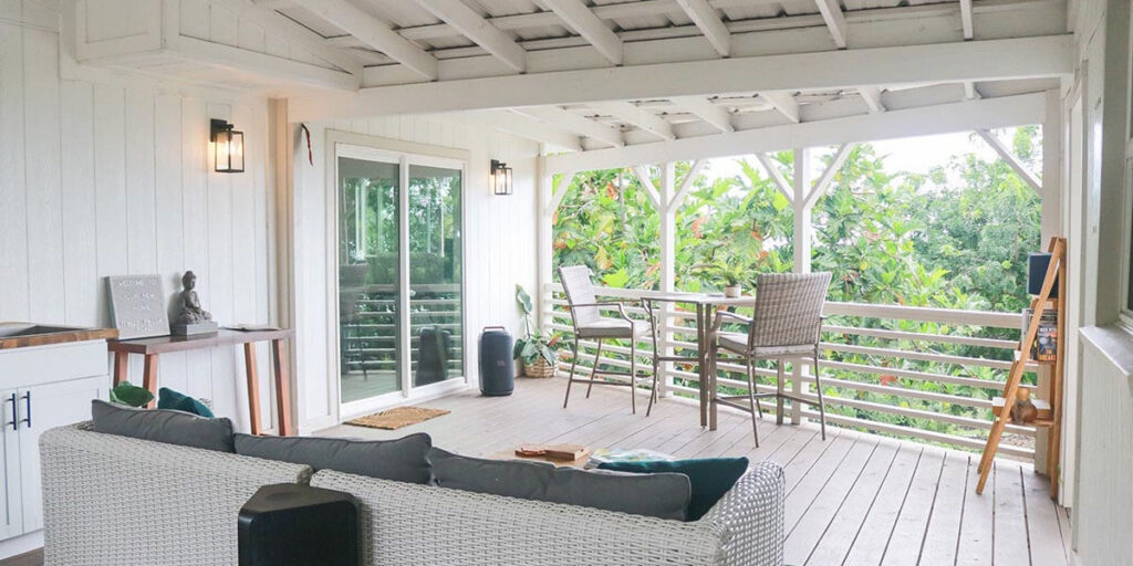 A cozy covered porch with wicker furniture overlooks a lush tropical garden.